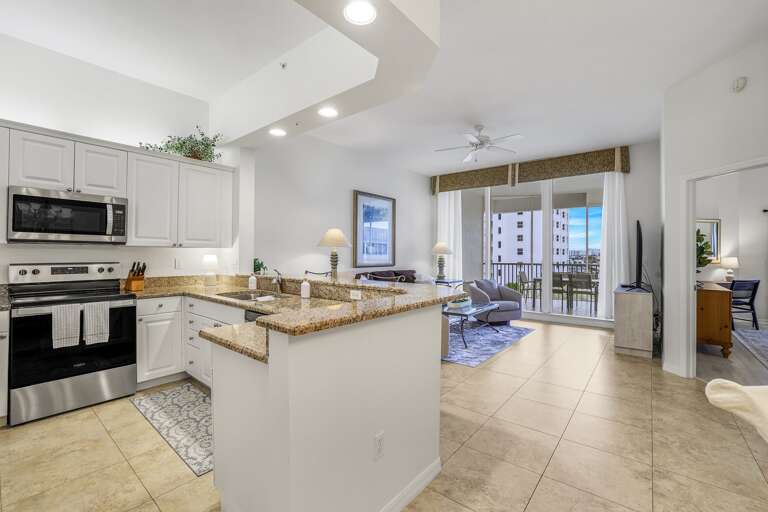 Bright, Spacious Living Space With Sleek Kitchen Leading To A Balcony