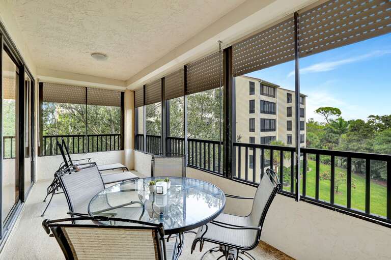Balcony With Black Chairs And Glass Table Overlooking Green Grounds