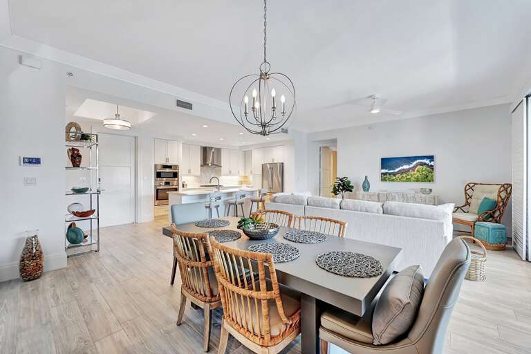 Bright, Breezy Living Space With Dining Area And Kitchen, Featuring White Walls And A Hanging Chandelier Bright, Breezy Living Space With Dining Area And Kitchen, Featuring White Walls And A Hanging Chandelier