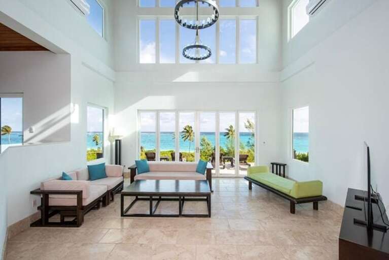 The great room, with 20-foot ceilings and a wall of tall glass Nana doors, opens onto a patio looking out over the beach and ocean.
