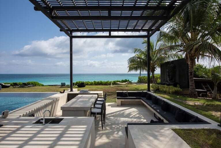 Swim-up bar, a dining area, and an outdoor kitchen equipped with a BBQ, sink and kitchen island with 4 bistro height chairs.