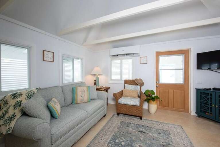 The main room features a queen bed and a living area with a large sofa, arm chairs, and a flat-screen TV