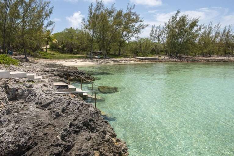 Calm turquoise water with a sandy bottom. Small private beach in the background.