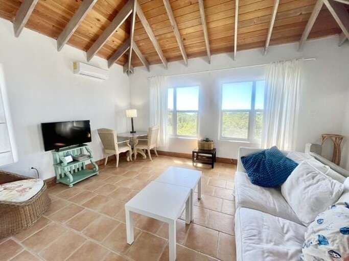 The Upstairs Living Area with panoramic ocean views, furnished with a pull-out sofa, wicker armchair, dining table for two, and a smart TV.