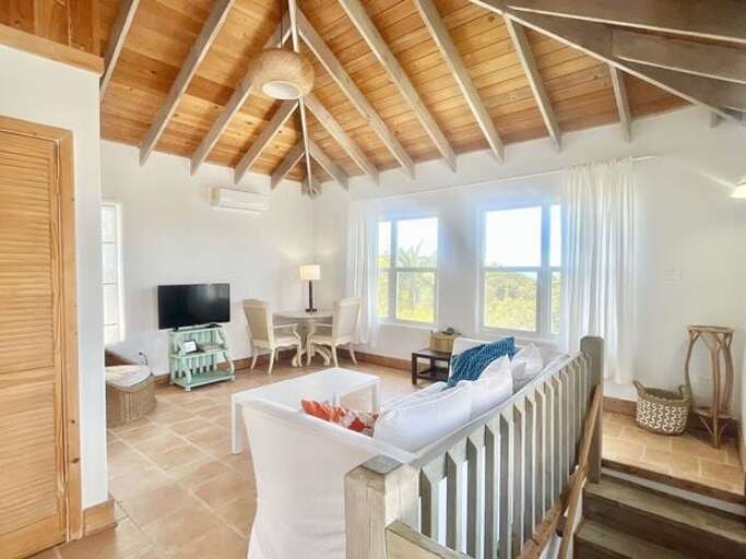 The Upstairs Living Area with panoramic ocean views, furnished with a pull-out sofa, wicker armchair, dining table for two, and a smart TV.