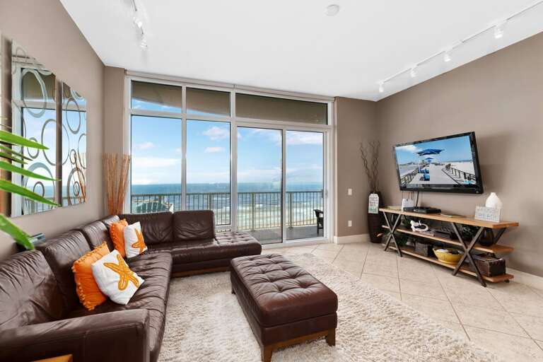 Living Room With Sea Views Through Large Windows, Brown Sofa, And Mounted TV