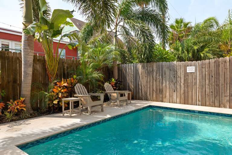 Sunny poolside seating surrounded by palm trees and vibrant greenery!