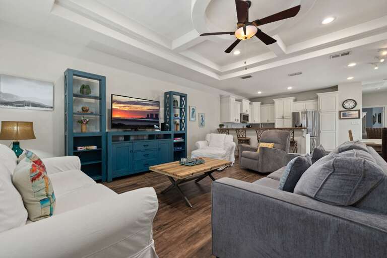 Bright and inviting living room featuring tray ceilings, coastal décor, and plenty of comfortable seating for the whole group