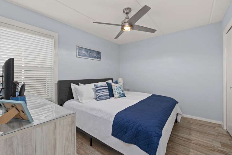 Inviting second bedroom with a king-size bed, ceiling fan, and bright coastal décor for a relaxing stay.