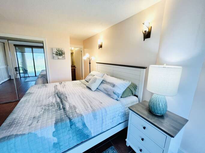 Alternate view of the primary bedroom showcasing comfortable furnishings, bedside lighting, and a relaxing coastal feel.