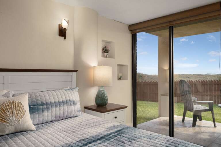 Bedroom With A Bed, Bedside Table, Lamp, Sliding Glass Door, And Patio View