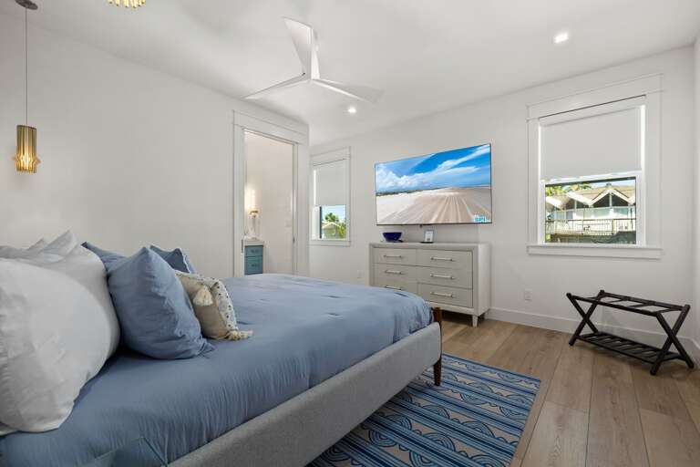 Retreat to the spacious primary bedroom featuring a comfortable king bed, mounted TV, and relaxing coastal décor.
