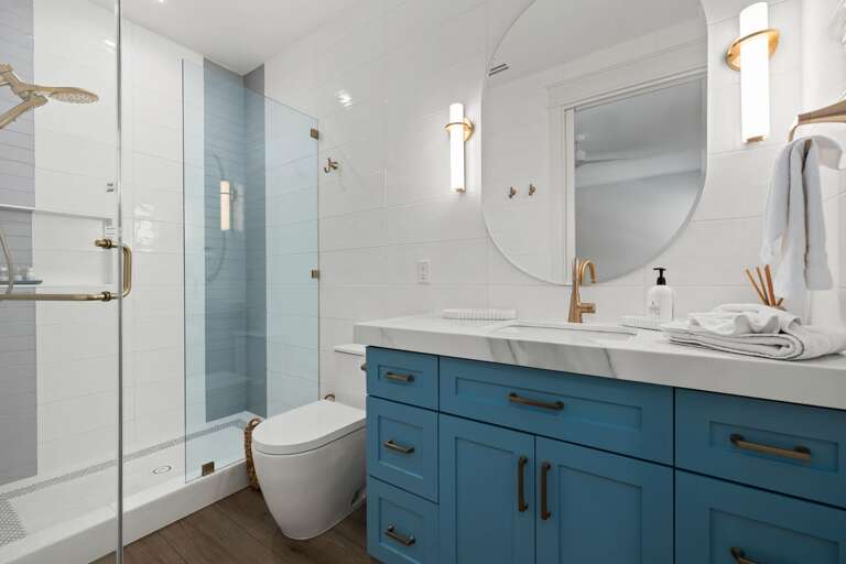 The primary ensuite bathroom features a spacious blue vanity, modern fixtures, and a glass-enclosed shower.