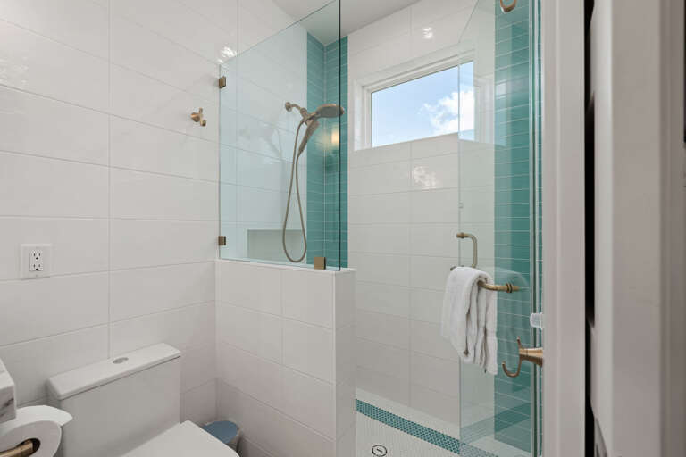 The updated guest bathroom features a glass-enclosed shower with beautiful turquoise tile accents.