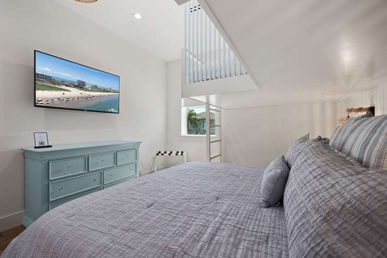 The spacious guest bedroom offers a queen bed, twin bunk beds, and a mounted TV for added entertainment.