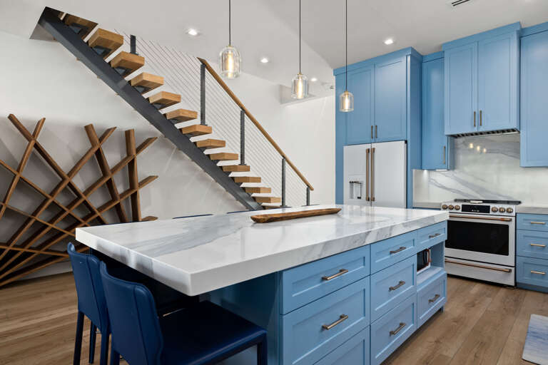 The open kitchen features a large island, beautiful blue cabinetry, and a stylish staircase leading upstairs.