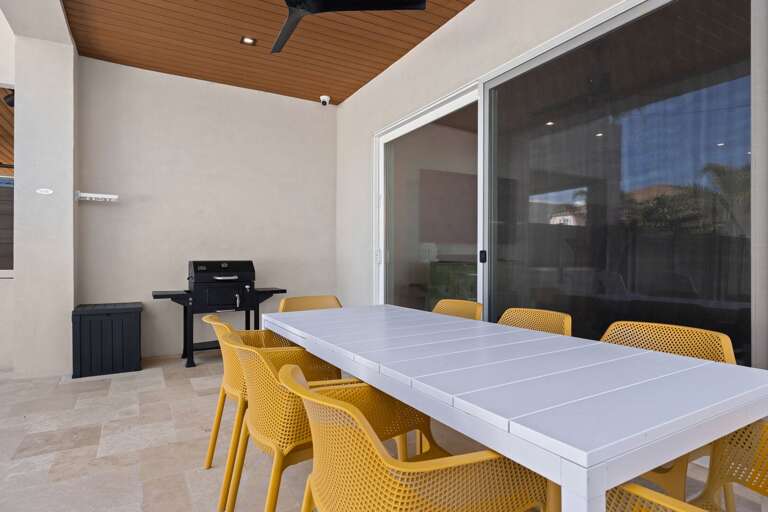 Dine outdoors beneath the covered patio, featuring a spacious table and seating overlooking the private pool area.