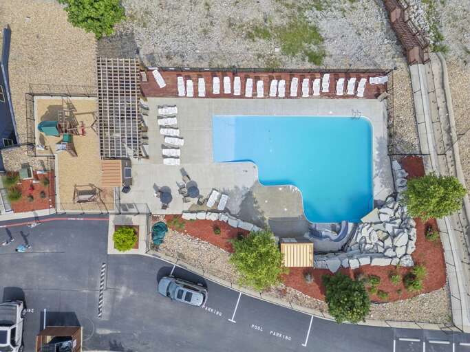 Aerial View Of A Pool By Pavement With Parked Cars And Loungers