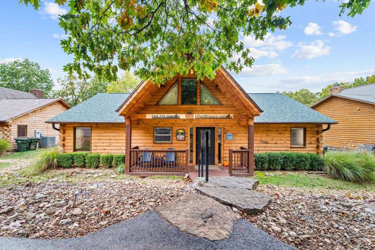 Log Cabin Under Lush Trees With A Porch And Paved Path