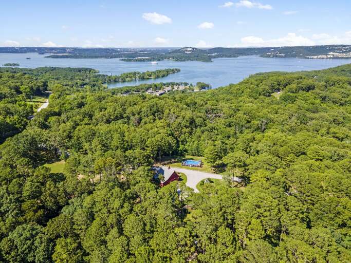 Aerial View Of A Large House Nestled In Lush Greenery Near A Lake With Winding Roads