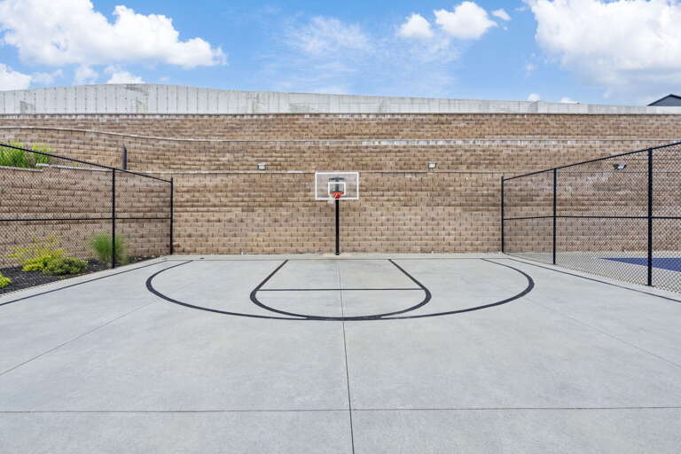 Basketball Court With A Backboard And Net, Enclosed By A Metal Fence And Brick Building Behind