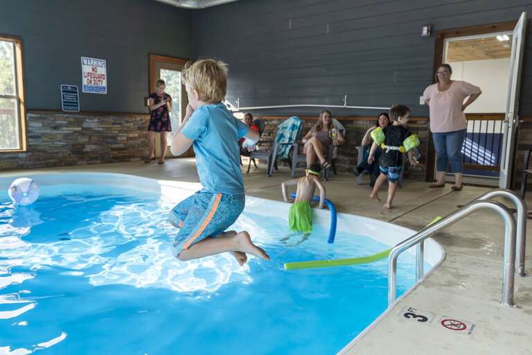 Child Cannonballing Into Indoor Pool While Family Watches