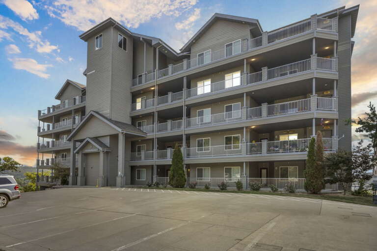 Vacation Rental Building Viewed At Dusk, Parking Prominent, Balconies Abound