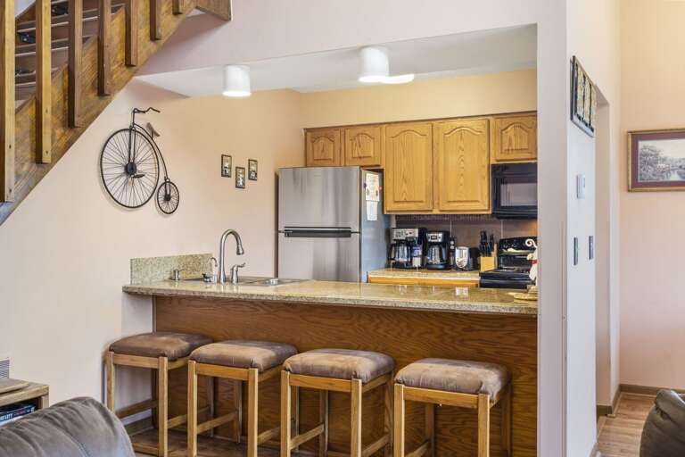 Kitchen With Wooden Cabinets, Stools, And Steel Appliances, Plus A Bike On The Wall Kitchen With Wooden Cabinets, Stools, And Steel Appliances, Plus A Bike On The Wall