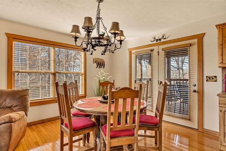 Dining Room With Wooden Table And Chairs, Chandelier, And Windows