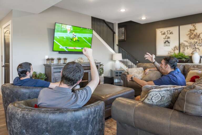 Three People Watching Football On TV In A Spacious Living Room