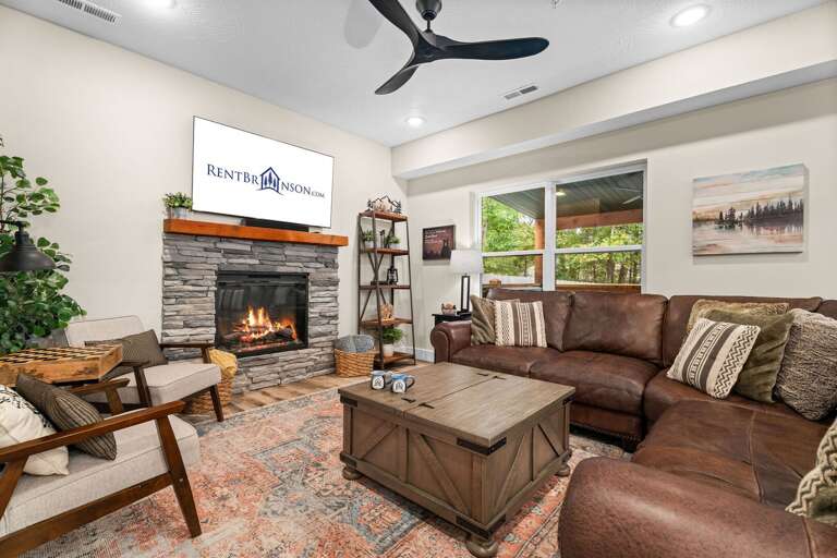 Living Room With Large Brown Sofa, Stone Fireplace, And Ceiling Fan