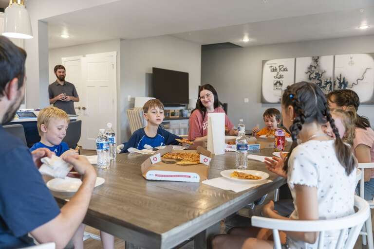 Family Gathers, Grins, And Dines Around Dining Table