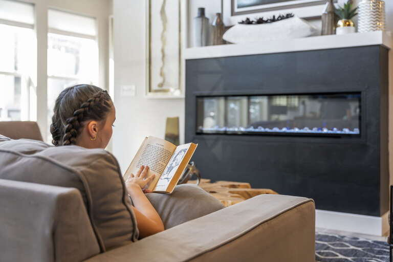 Woman Reading Beside Black Fireplace