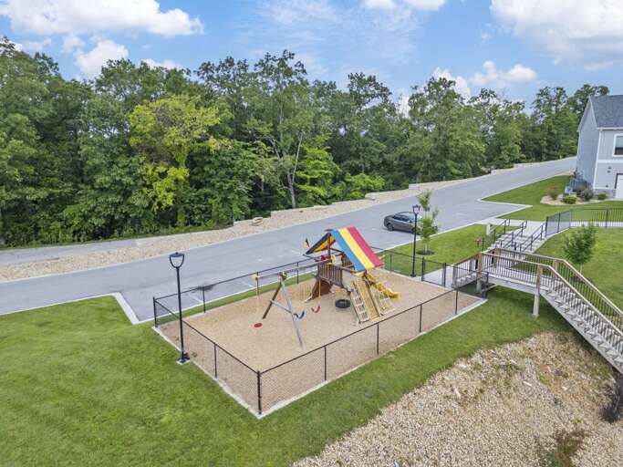 Aerial View Of Playground With Slide And Swings, Surrounded By Green Grass And Roads
