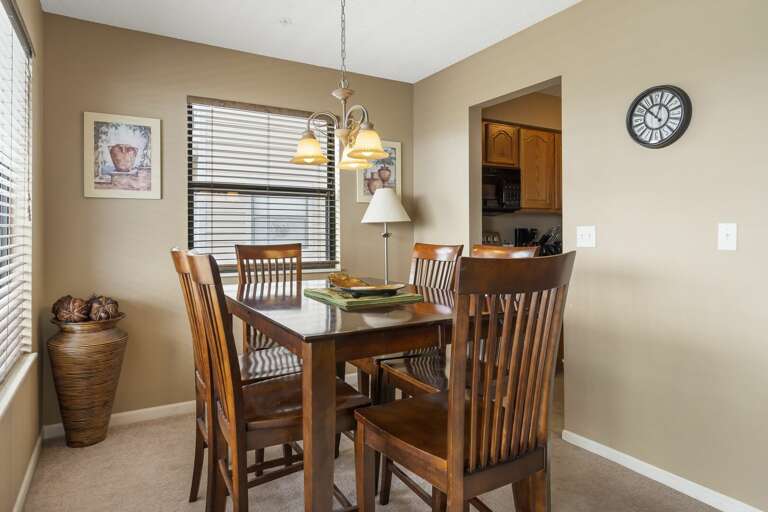 Dining Room With Wooden Table And Chairs, Clock On Wall, And Framed Picture