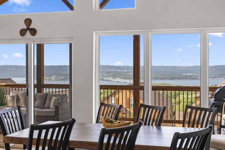 Interior View Of A Dining Area With A Large Table, Chairs, And A Lake View Through Windows