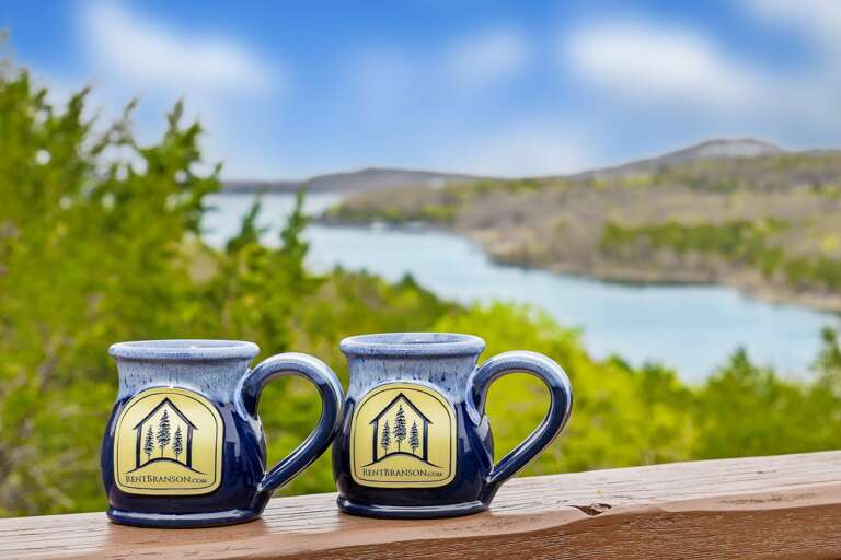 Two Souvenir Mugs With Scenic Lake View In The Background Two Souvenir Mugs With Scenic Lake View In The Background