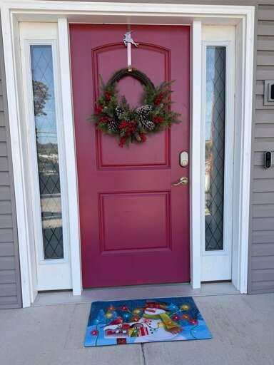 Red Door Decked With Circular Christmas Wreath, White Frame, Welcome Mat Below