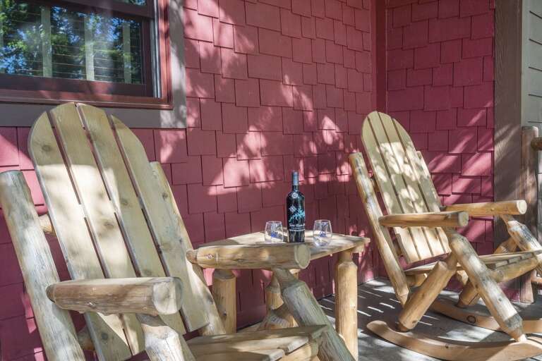 Two Wooden Chairs On Vacation Rental Porch With A Bottle And Glasses