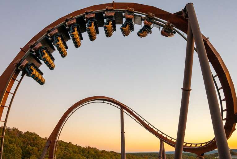 Rollercoaster Riders Rounding A Curve At Sunset