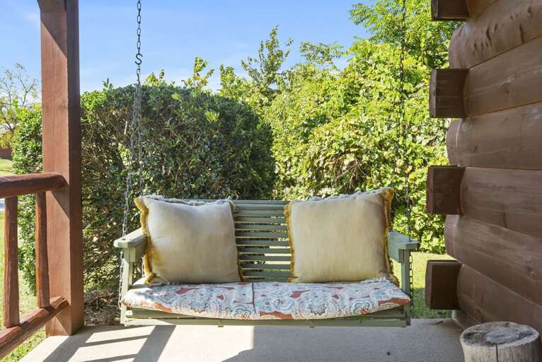 Swing Bench On Porch Of A Log Cabin Surrounded By Greenery Swing Bench On Porch Of A Log Cabin Surrounded By Greenery