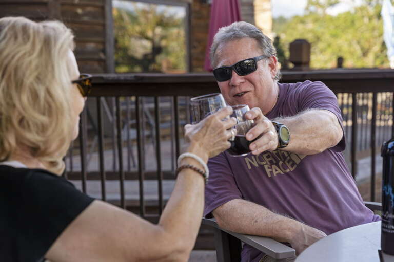 Mature Couple Toasting Drinks At A Wooden Table Outdoors