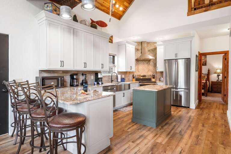 Polished Kitchen Space With Stainless Steel Appliances, Bar Stools, And Wood Flooring