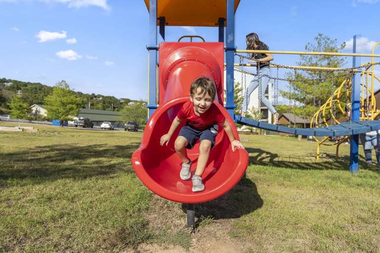 Boy Beaming, Sliding Swiftly Down Bright Red Playground Spiral Slide Boy Beaming, Sliding Swiftly Down Bright Red Playground Spiral Slide