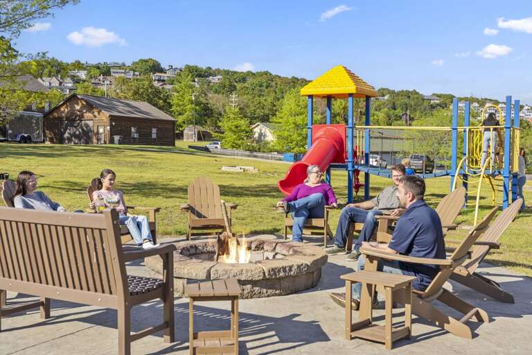 Group Gathering Around A Fire Pit, Playground In Park Setting Group Gathering Around A Fire Pit, Playground In Park Setting