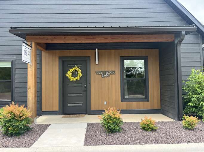 Facade Featuring Dark Siding, Contrasting Light Wooden Panel, Front Door With Yellow Wreath