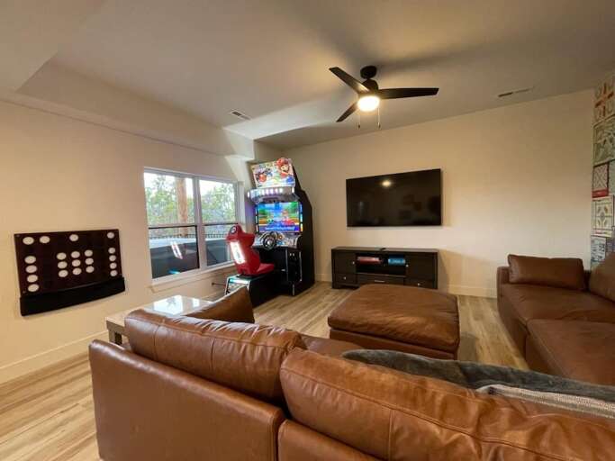 Living Room With Leather Sofas, Arcade Game, And Wall-mounted TV