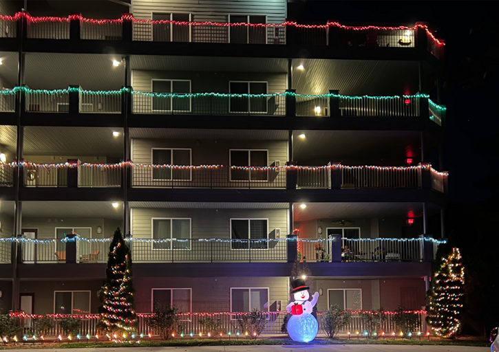Building Brightened By Balcony Lights, Festive Fir Trees Flanking Luminescent Snowman