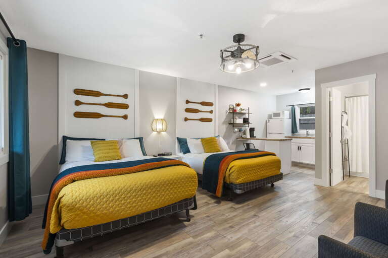 Bright Bedroom With Two Beds, Wooden Accents, And Adjacent Kitchen Area In A Vacation Rental Bright Bedroom With Two Beds, Wooden Accents, And Adjacent Kitchen Area In A Vacation Rental
