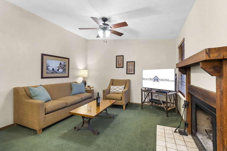 Living Room With Tan Sofa, Large Screen TV, And Fireplace